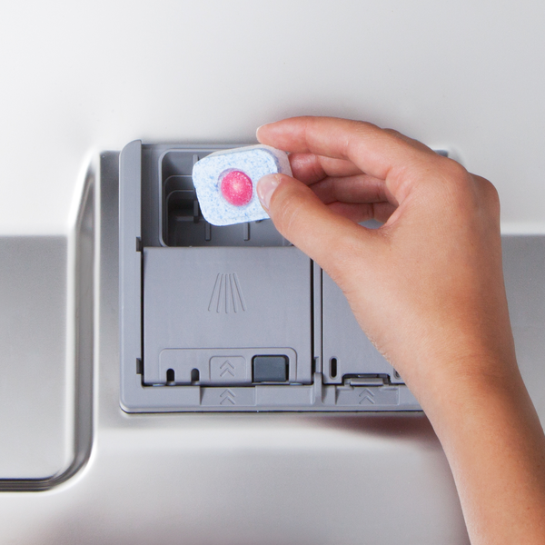 Hand placing a dishwasher tablet into a dishwasher detergent dispenser.